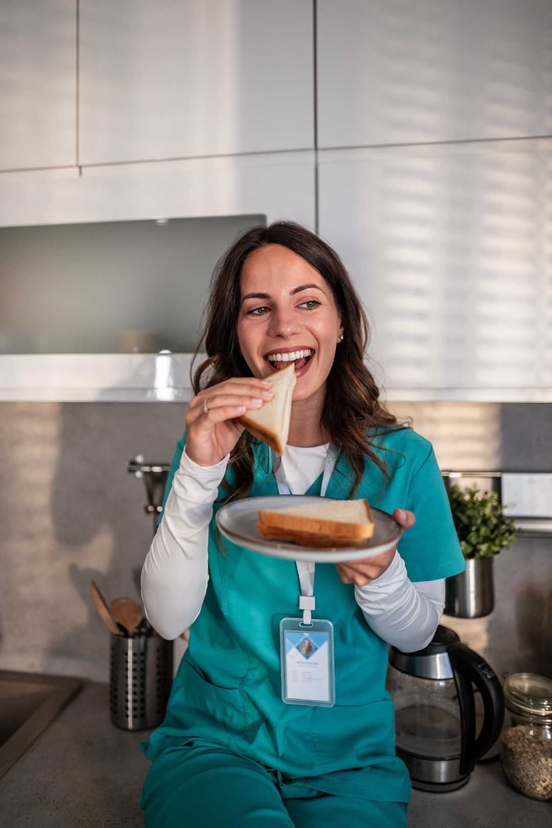 A woman in a medical facility in Chicago, IL, sitting on a counter in the break room enjoying a hearty sandwich during her break.
