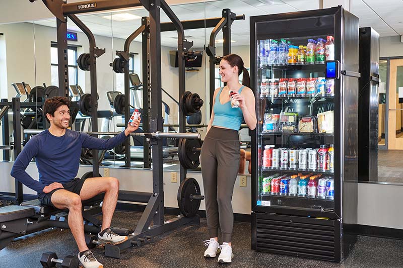 A man and woman in a gym, taking a break and enjoying items from Avcoa Vending Smart Coolers in Chicago, IL.