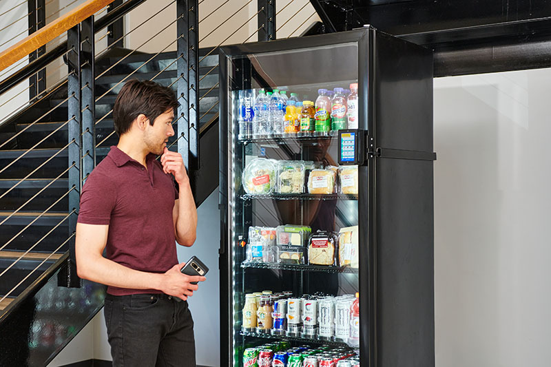 A young man decides which items to select from a modern smart cooler from Avoca Vending in Chicago, IL.