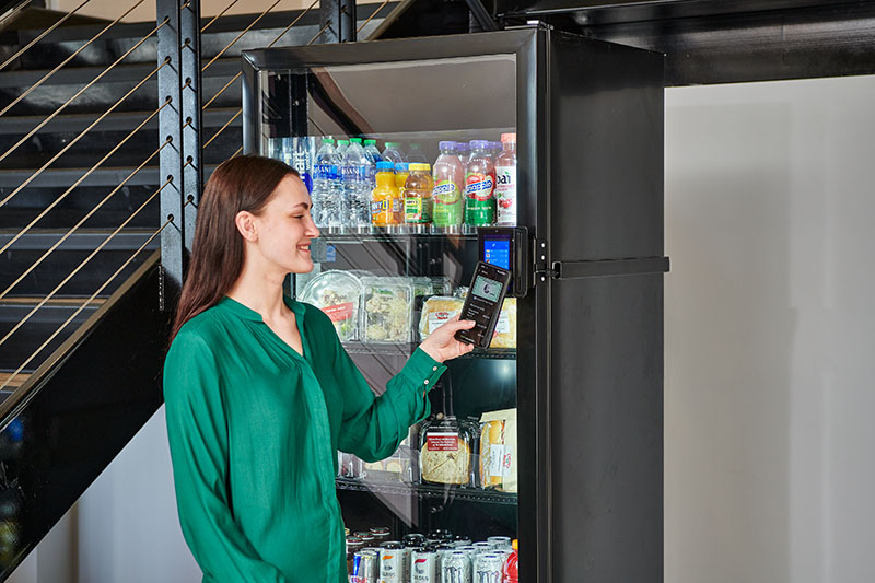 A young woman pays for her selection at a modern smart cooler provided by Avoca Vending in Chicago, IL.